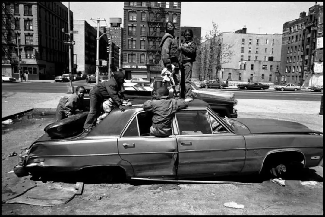 USA. New York City. 1987. Harlem street scene. Child playing in an unfed car.