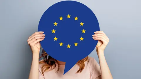 woman holds blank white speech bubble with european union flag isolated over grey studio background. News information channel concept